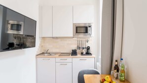 Pieni, käytännöllinen keittiö, jossa on valkoiset kaapit, mikroaaltouuni, kahvinkeitin ja hedelmäkulho työtasolla.