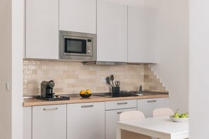 Eine kleine Küche mit einer Mikrowelle, einer Kaffeemaschine und einer Obstschale auf der Arbeitsfläche.