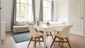 Ein modernes Wohnzimmer mit einem weißen Sofa, einem Esstisch mit Stühlen und einem großen Fenster mit Vorhängen.