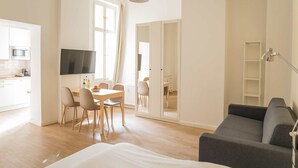 Ein modernes Zimmer mit einem Bett, einem grauen Sofa, einem Fernseher, einem Esstisch mit Stühlen und einer Küchenzeile.