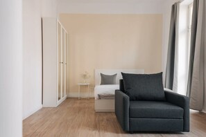 Een minimalistische slaapkamer met een bed, een grijze fauteuil, een klein bijzettafeltje en een kledingkast.