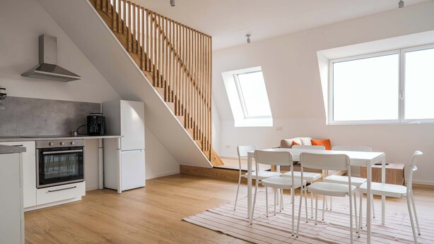 Eine moderne Küche mit Einbauofen, ein Essbereich mit weißen Stühlen und einem Tisch sowie eine Holztreppe.