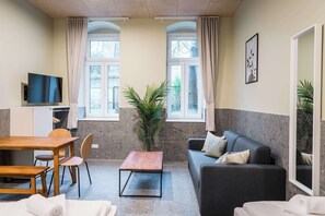 Ein Zimmer mit Esstisch, Stühlen, einer Couch, einem Fernseher und einer Zimmerpflanze.