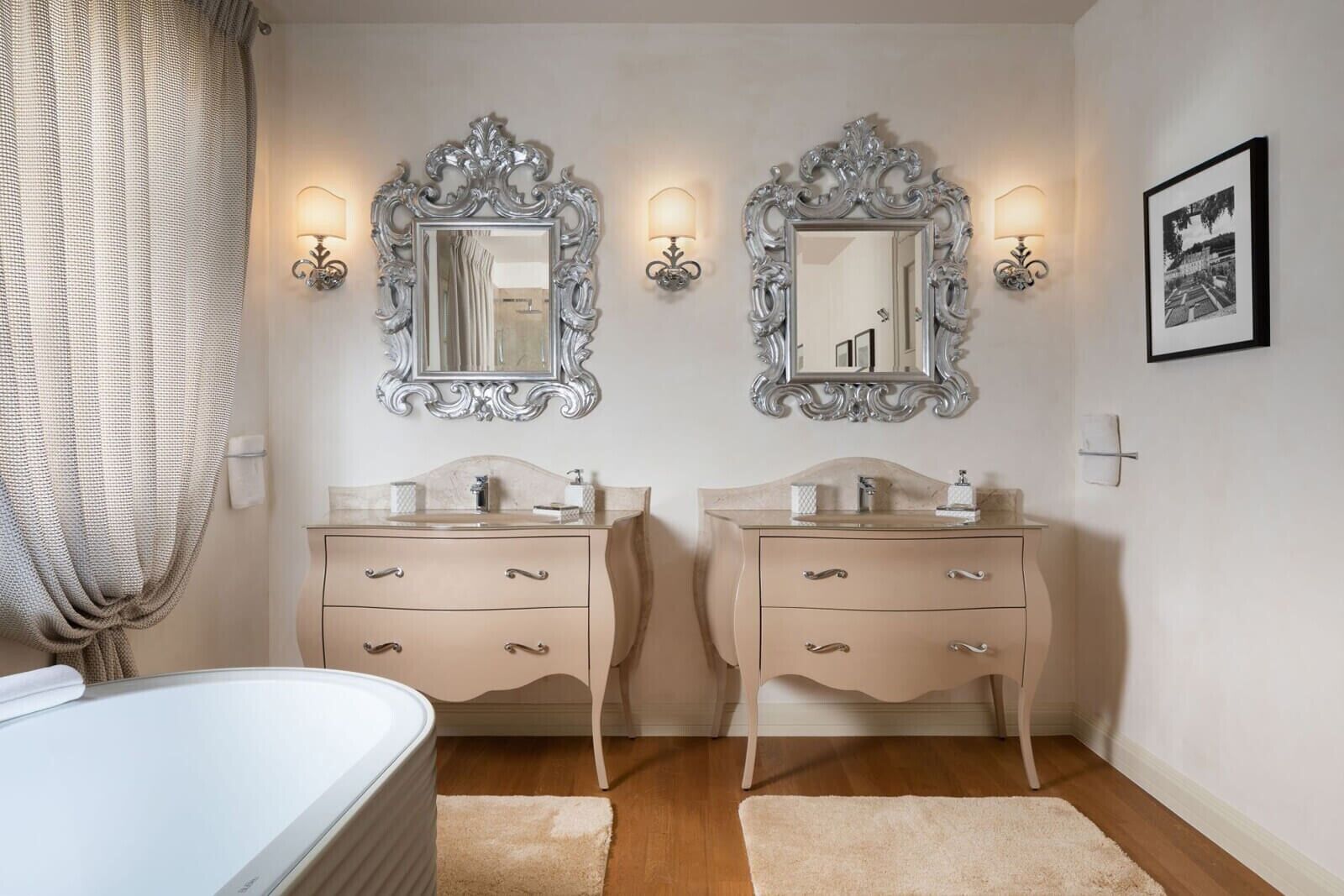 A hotel room with two bedside tables, a bed, a large mirror, wall sconces, and a framed picture.