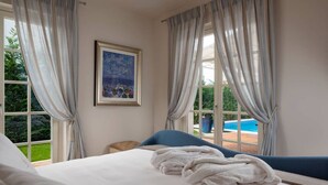 A bedroom with a bed, a blue chair, a painting, and a view of a swimming pool. - Villa Giulia – Luxury villa for up to 6 guests with heated private pool in peaceful surroundings. (Vabriga)