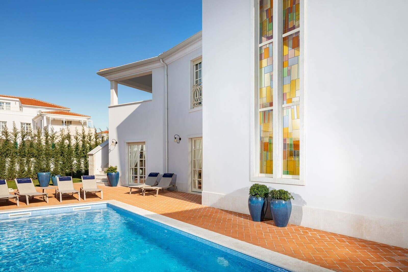 A swimming pool with lounge chairs, a white building with a balcony, and a large stained glass window.