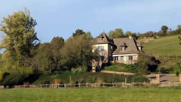 Une maison avec une façade en pierre, une grande pelouse et une clôture en bois.