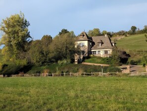 Uma casa com fachada de pedra, um gramado amplo e uma cerca de madeira.