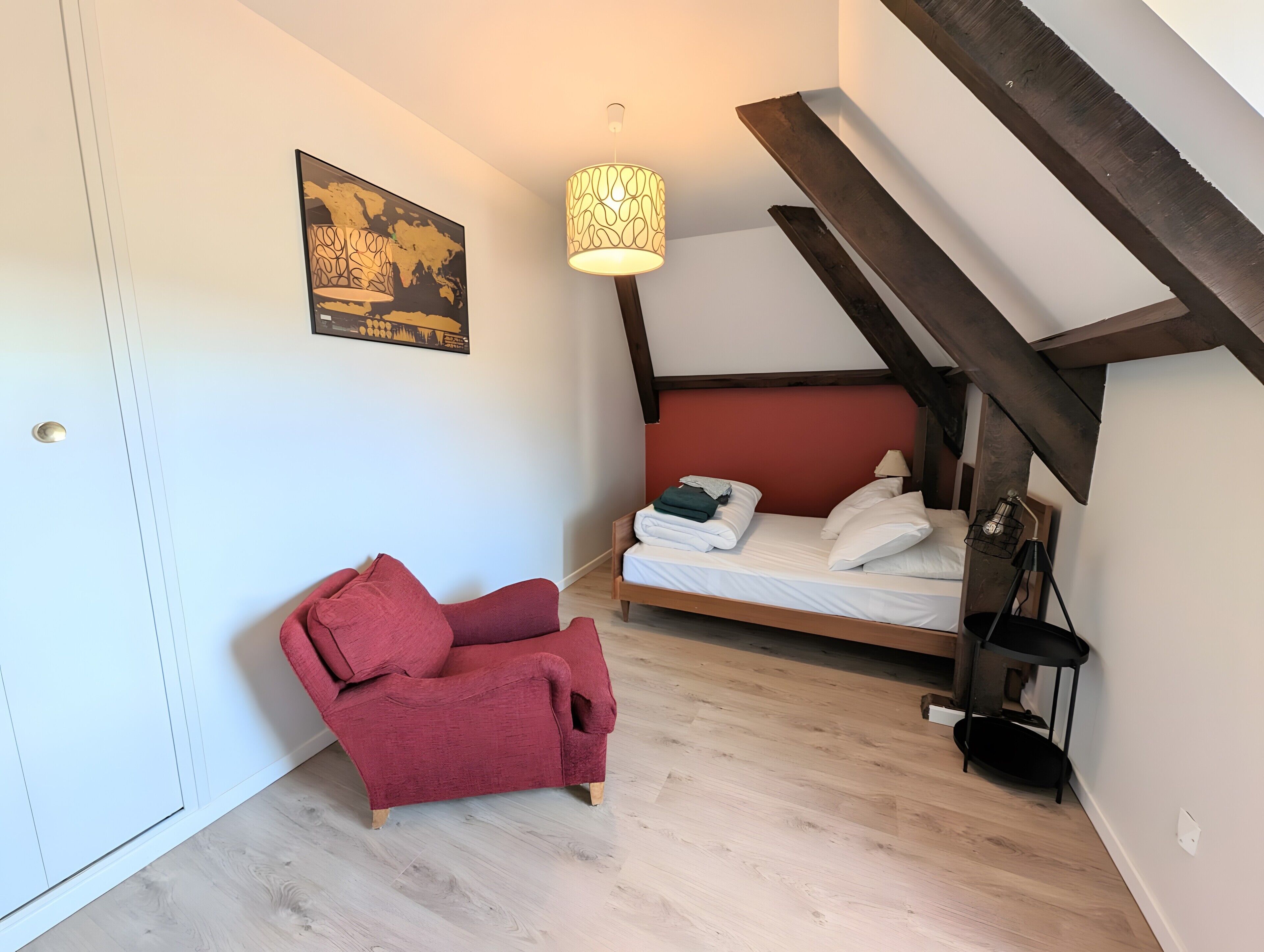 Une chambre à coucher avec un lit, une chaise rouge, une lampe suspendue et un tableau au mur.