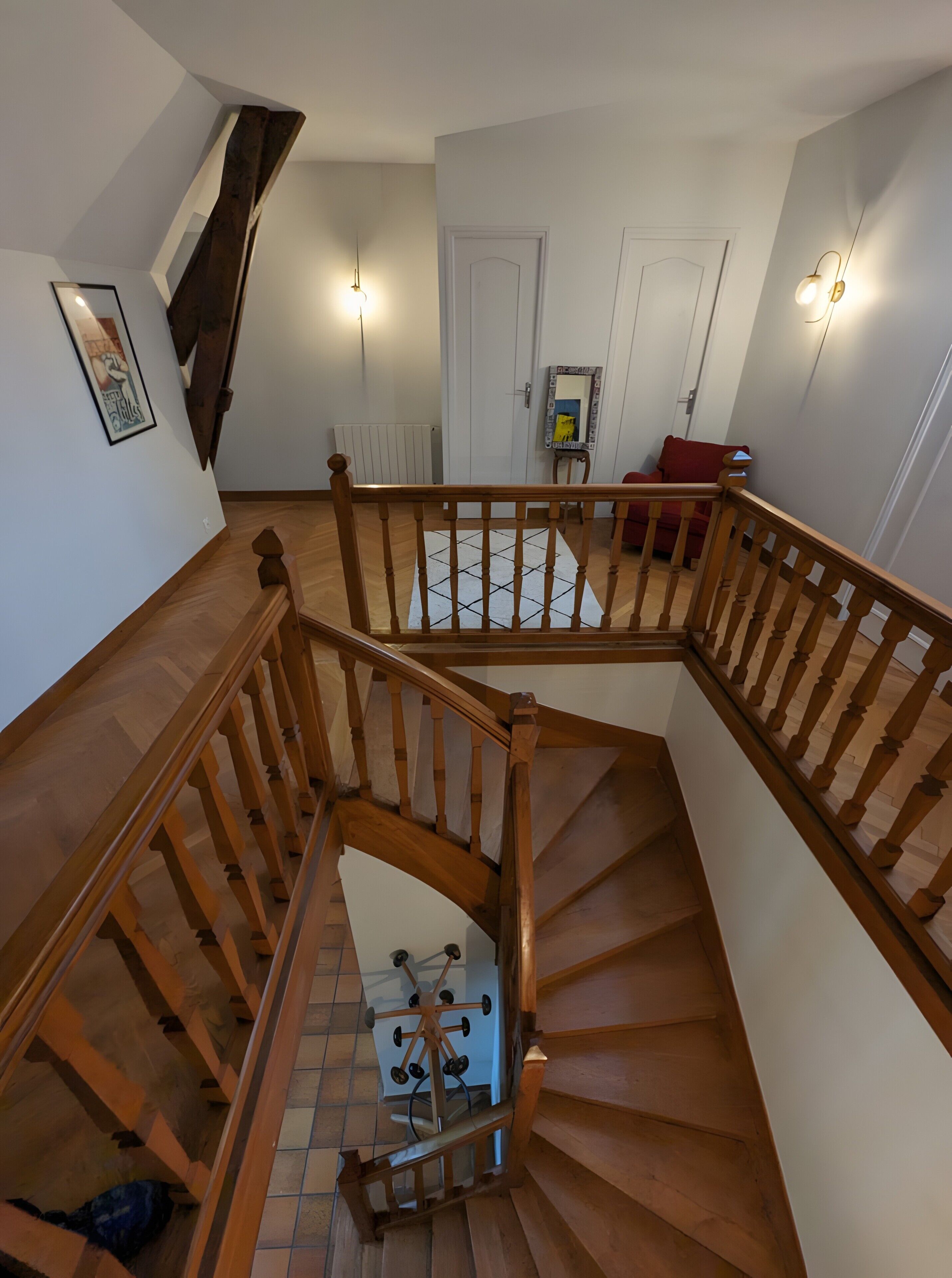 Un escalier en bois avec une rampe, un radiateur, une porte et une chaise rouge dans une pièce aux murs blancs.