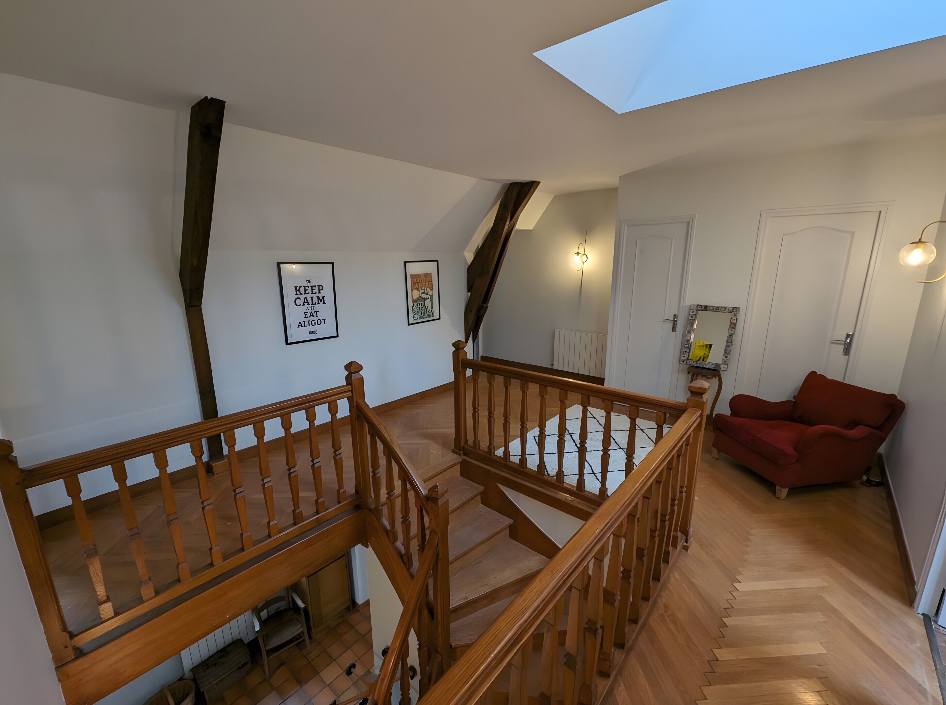 A spacious loft with a wooden staircase, a red armchair, and a skylight.