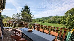 Une terrasse extérieure avec une table et des chaises, une vue sur un paysage verdoyant et une clôture en bois.