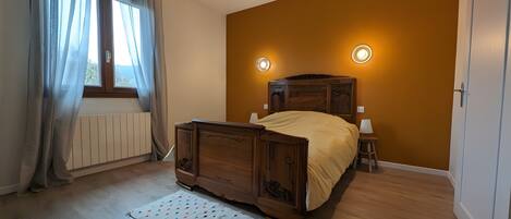 Un dormitorio con una cama de madera, un radiador, una ventana con cortinas y dos luces fijadas a la pared.