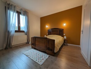 A bedroom with a wooden bed, a radiator, a window with curtains, and two wall-mounted lights. - Spacious Charming House for 12 – Vineyard Views & Tranquility for Families/Friends/Sports Groups (Clairvaux-d'Aveyron)