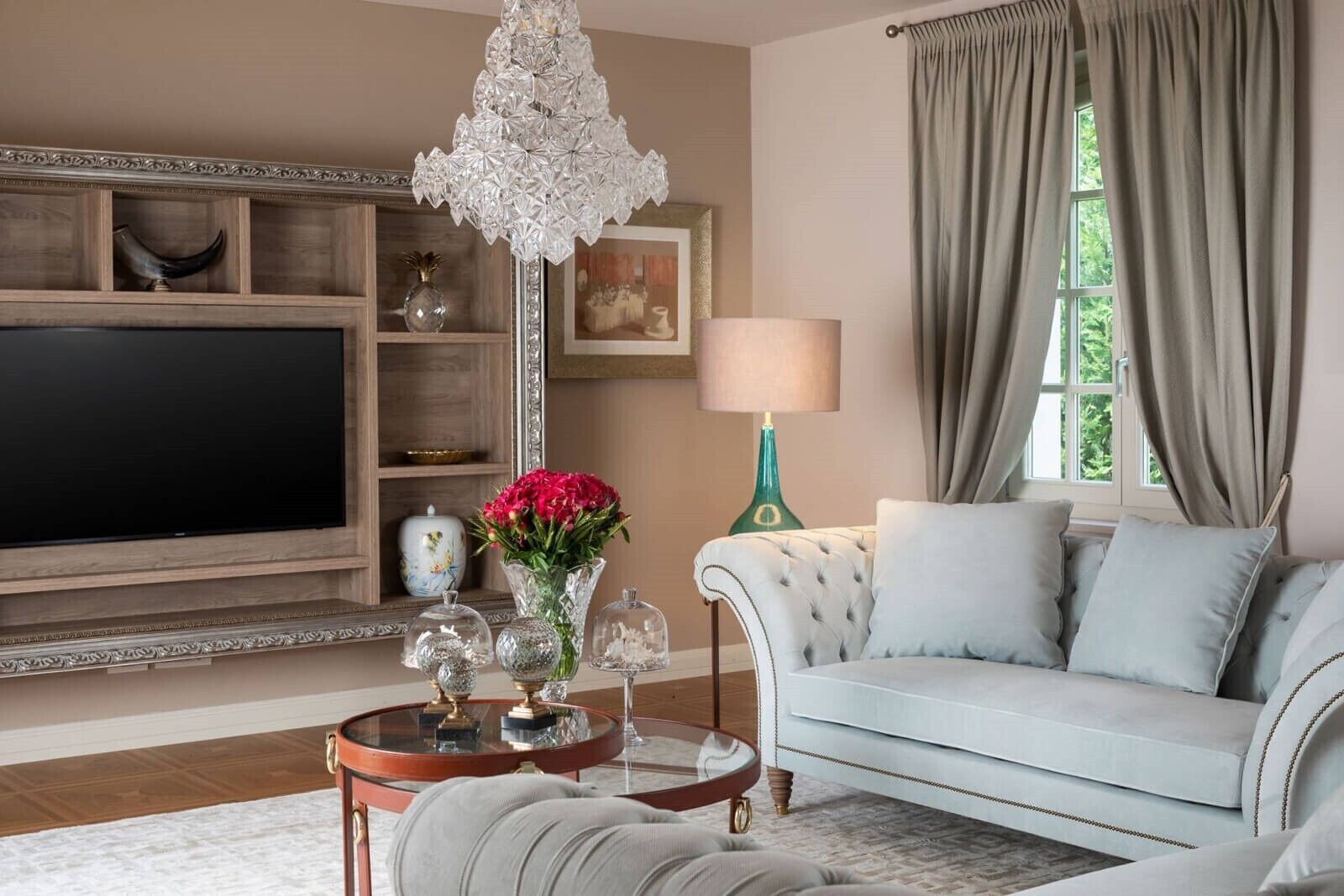 A living room with a television, a chandelier, a sofa, a lamp, and a window with curtains.
