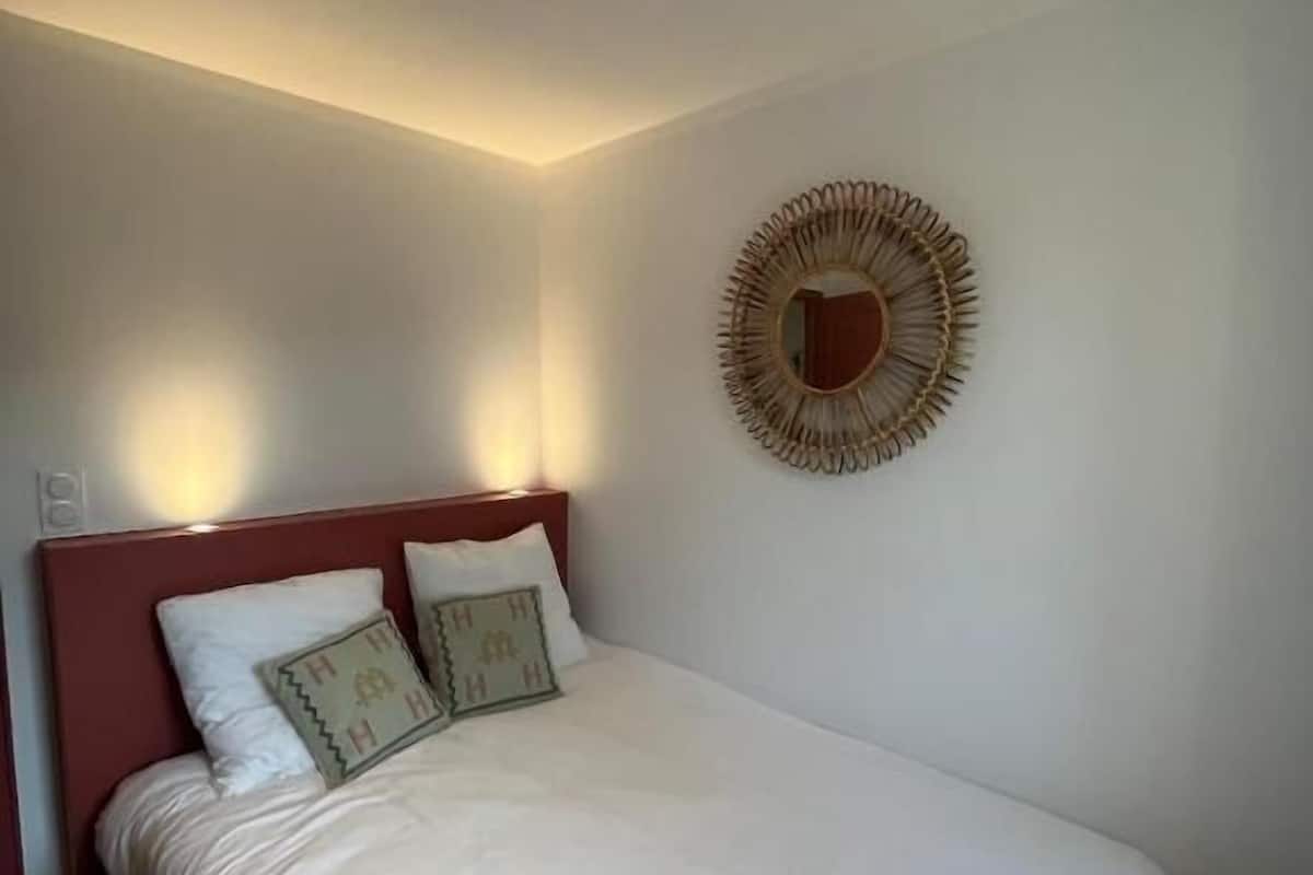 A bedroom with a bed, pillows, a headboard, a wall-mounted mirror, and a ceiling light.