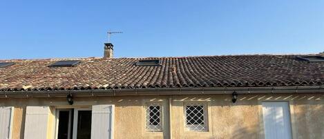 A building with a tiled roof, a chimney, and a door with shutters.