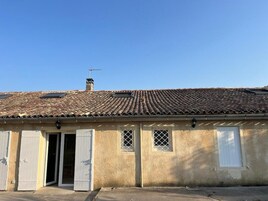 Un edificio con techo de tejas, chimenea y puerta con contraventanas.