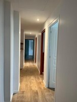 Un pasillo con piso de madera, paredes blancas y puertas que dan a otras habitaciones.