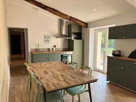 Una cocina con mesa y sillas de madera, microondas, horno y armarios verdes.