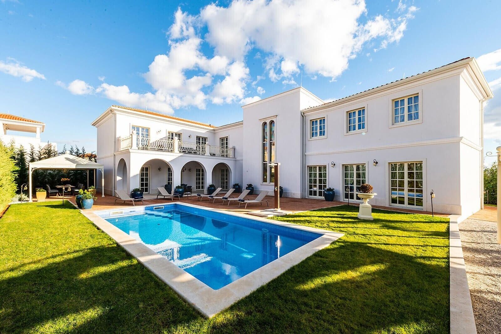 A large white house with a swimming pool, multiple balconies, and a covered patio area.