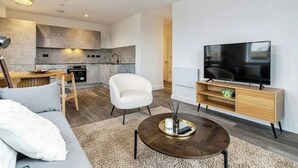 Un salon moderne comprenant un canapé, une table basse, un téléviseur et un coin cuisine avec des placards et une table à manger.