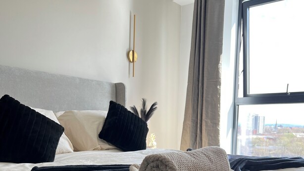 Une chambre d’hôtel avec un grand lit, une vue sur la ville par la fenêtre et un luminaire moderne fixé au mur.
