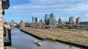 Une rivière avec un bateau, une vue sur les gratte-ciel d’une ville et un immeuble doté d’un balcon.