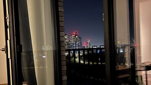 Une vue depuis un balcon, donnant sur une ville illuminée la nuit, avec des bâtiments dont les sommets sont éclairés et un ciel dégagé.