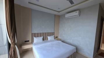Una habitación de hotel con una cama, ventilador de techo, aire acondicionado y ventana con cortinas.