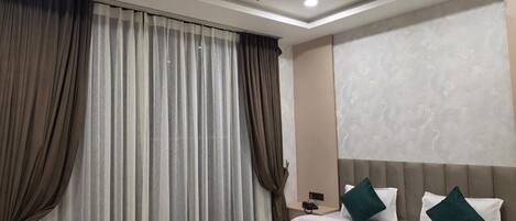 Une chambre d’hôtel avec un lit, des rideaux, un ventilateur de plafond et une table de chevet.