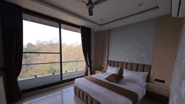 Una camera da letto con un letto grande, una ventola a soffitto, una finestra con tende e vista sugli alberi.