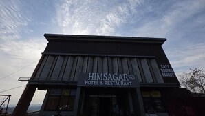 Un edificio con un cartello che recita 'HIMSAGAR HOTEL & RESTAURANT' e 'CAFE ROOMS BANQUET', che indica un albergo e ristorante con caffetteria e spazi per banchetti.