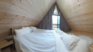 A room with a wooden sloped ceiling, a bed with white bedding, a window with curtains, and a small bedside table. - Mood villa kazbegi is city centre of Stepantsminda, with mountimes view. For you (Stepantsminda)