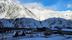 A snow-covered mountain with a small settlement, including houses and a fence. - Mood villa kazbegi is city centre of Stepantsminda, with mountimes view. For you (Stepantsminda)