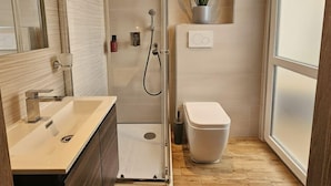 A modern bathroom with a glass shower enclosure, a sink, a toilet, and a potted plant. - ARYA Cagliari (Cagliari)