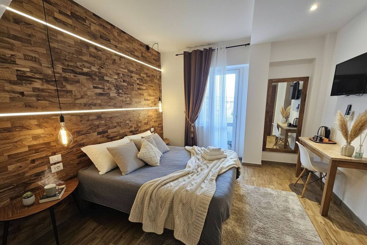 Ein modernes Schlafzimmer mit einer Holzwand, einem Bett mit Decke, einem Nachttisch mit Lampe und einem Schreibtisch mit Stuhl.