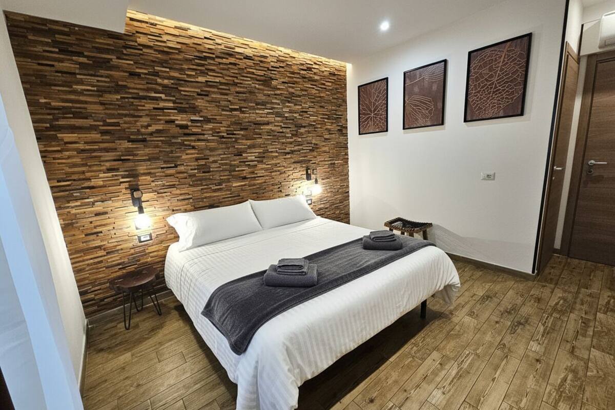 Ein modernes Schlafzimmer mit einer Holzvertäfelung, einem Bett mit weißen Bettwäsche, zwei Wandleuchten und drei gerahmten Kunstwerken.