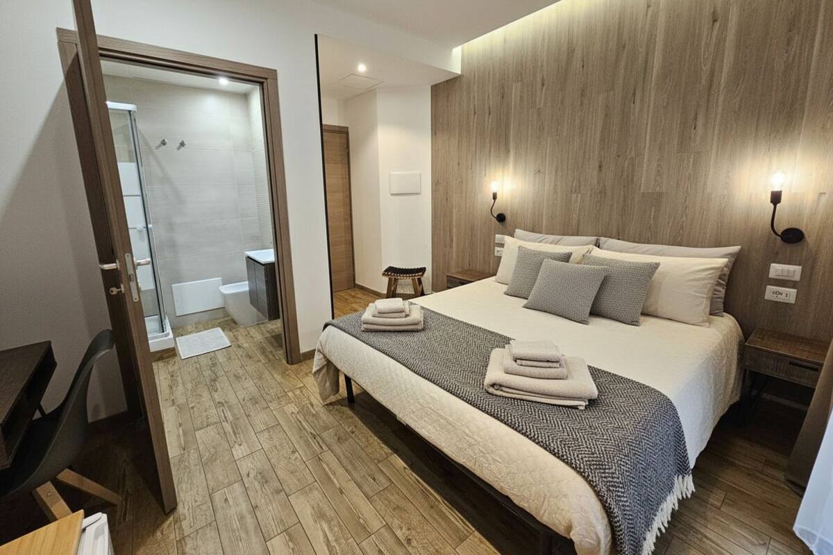 Ein modernes Hotelzimmer mit einem Holzkopfende, einem großen Bett mit Kissen, einem Nachttisch und einem Beistelltisch.