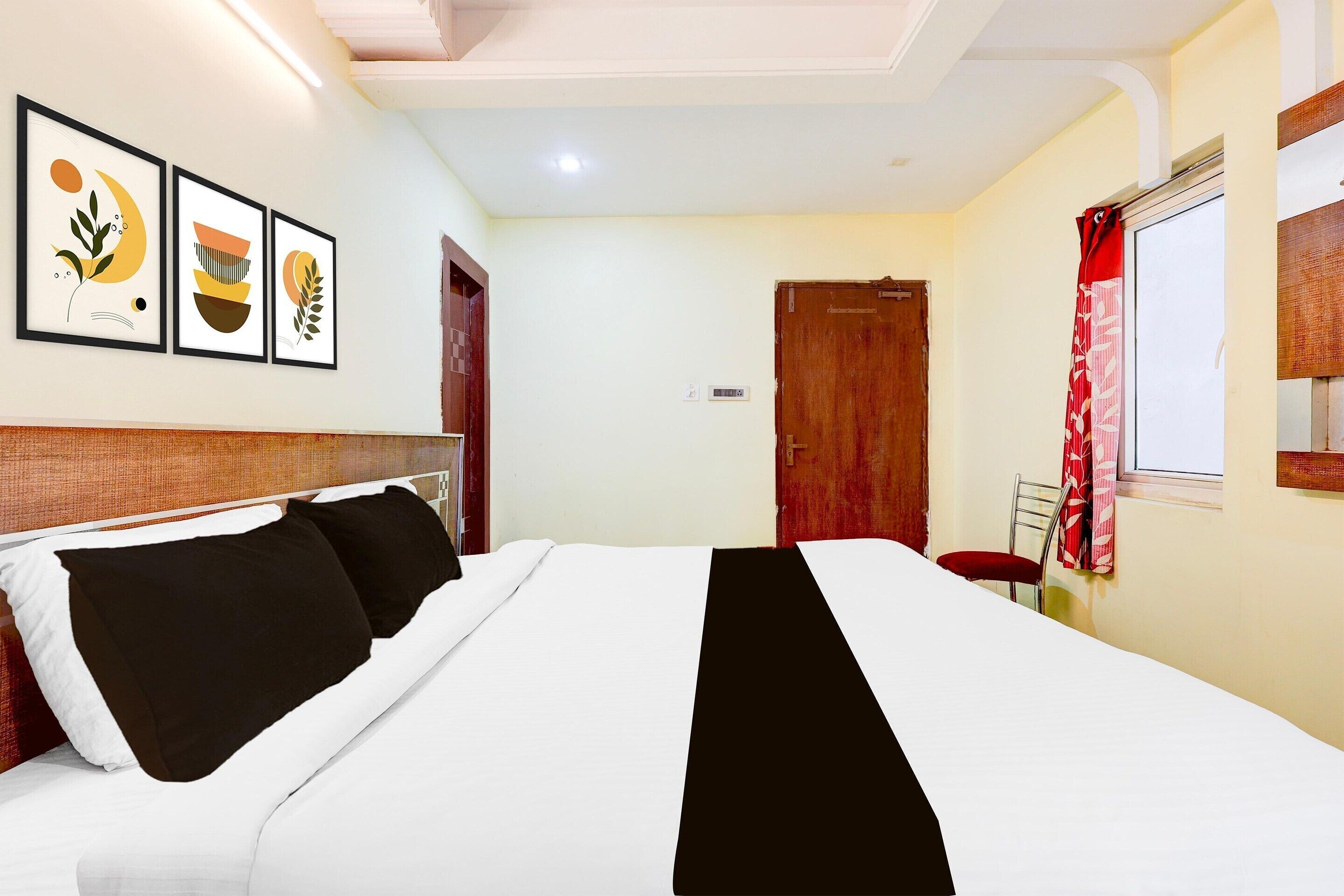 A hotel room with a bed, a chair, a door, and three framed artworks on the wall.