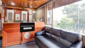 A reception area with a wooden reception desk, a black leather sofa, and a view of trees through large windows.