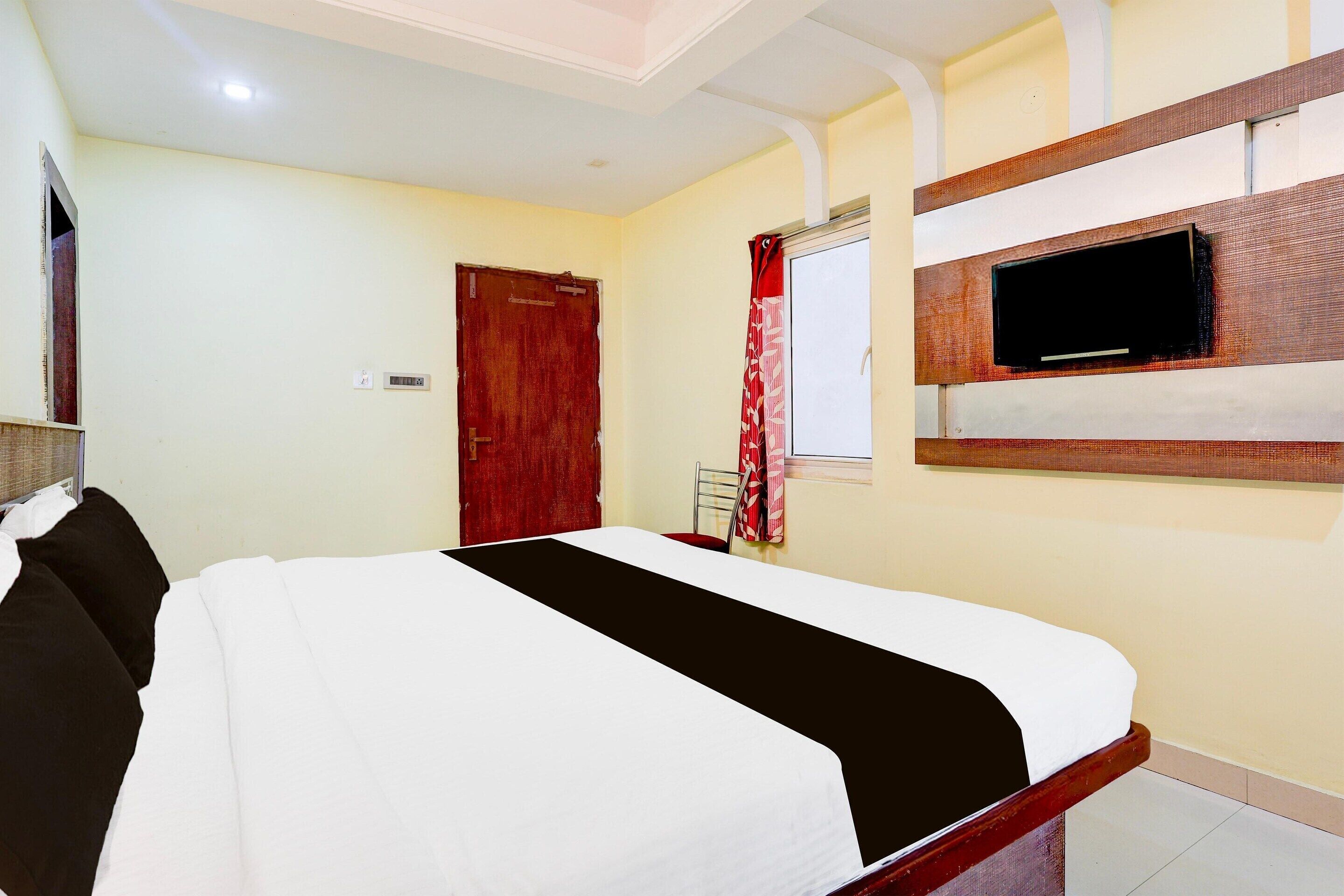 A bedroom with a bed, a wooden headboard, a television mounted on the wall, and a door.