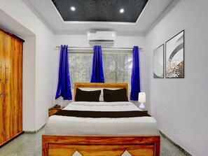 A bedroom with a bed, a wooden wardrobe, a window with curtains, an air conditioning unit, and two wall-mounted artworks. - Deluxe Seven Hills Aurangabad (Chhatrapati Sambhajinagar)