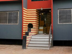 A building with a red and yellow striped wall, a set of stairs leading to a door, and barred windows. - Deluxe Seven Hills Aurangabad (Chhatrapati Sambhajinagar)