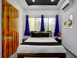 A bedroom with a bed, a wardrobe, a window with curtains, an air conditioning unit, and artwork on the wall. - Deluxe Seven Hills Aurangabad (Chhatrapati Sambhajinagar)