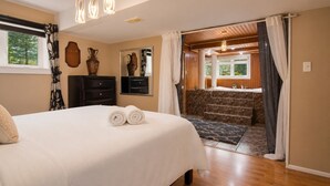 Een slaapkamer met een bed, twee nachtkastjes, een kaptafel, een spiegel en een badkamer met douche en wastafel.