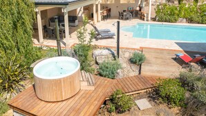 Un patio trasero con un jacuzzi, una piscina y un porche cubierto con mobiliario exterior.