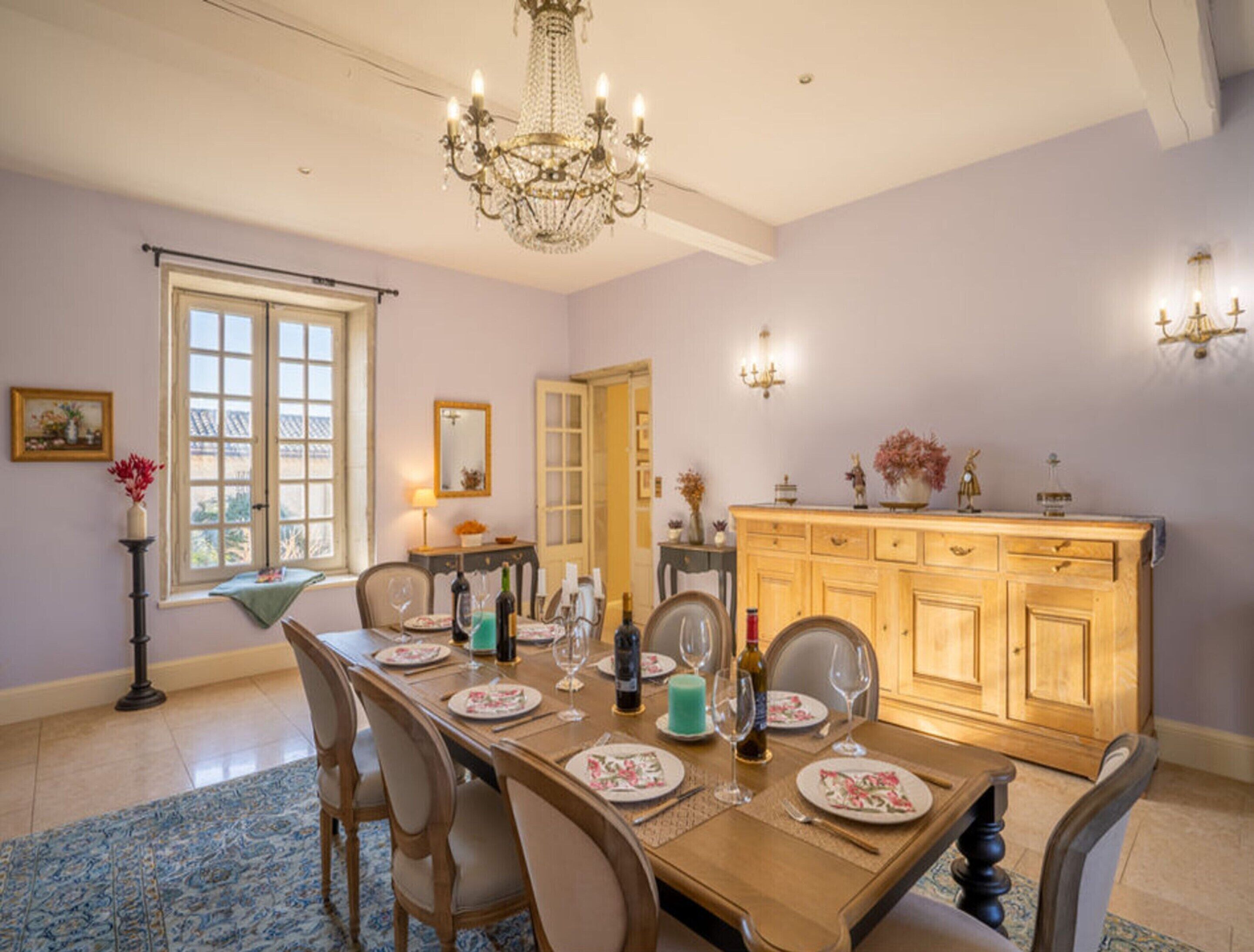 A dining room with a wooden table set for four, a chandelier, and a wooden cabinet with decorative items.