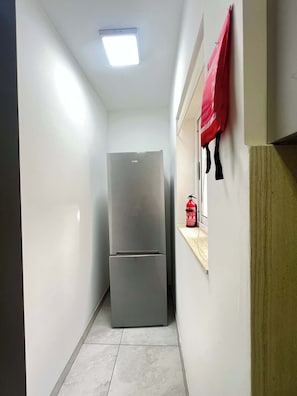 A narrow hallway with a double-door refrigerator, a fire extinguisher, and a red bag on a shelf. - Swieqi Modern 3 BDR Flat by PMI Malta (Is-Swieqi)