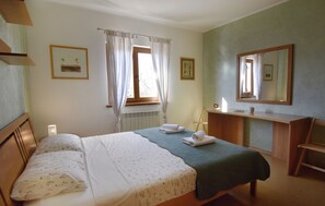 Un dormitorio con cama, escritorio, silla, ventana con cortinas y un radiador.